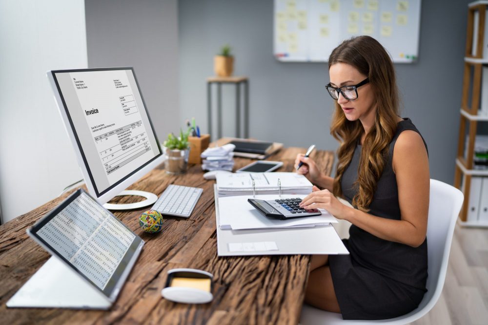 femme avec des lunettes faisant ses papiers et calculs sur son bureau